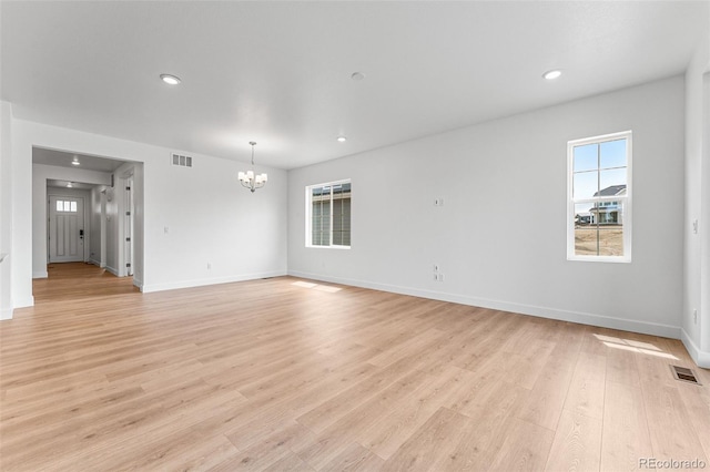 spare room featuring plenty of natural light, light hardwood / wood-style flooring, and a notable chandelier