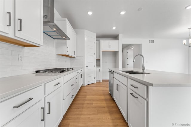 kitchen with white cabinetry, a center island with sink, stainless steel appliances, wall chimney range hood, and sink