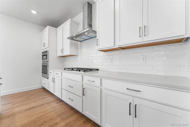 kitchen featuring white cabinetry, wall chimney range hood, light hardwood / wood-style flooring, and stainless steel appliances