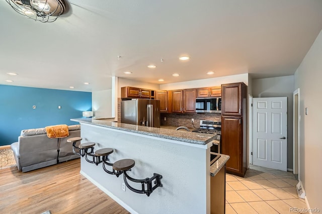 kitchen with dark stone counters, a breakfast bar, appliances with stainless steel finishes, open floor plan, and backsplash