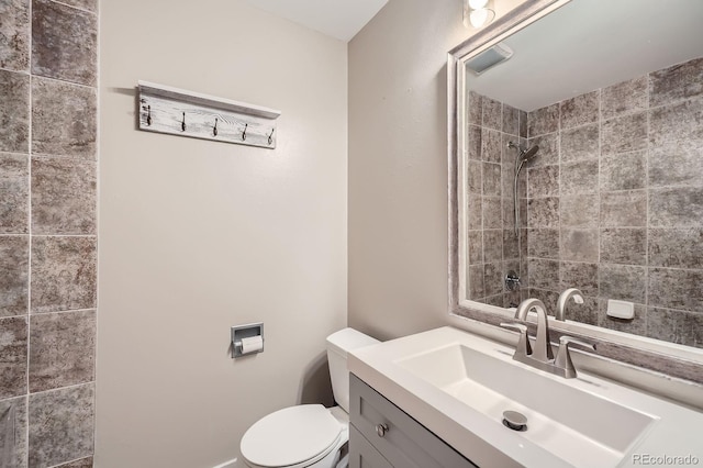 bathroom featuring toilet, tiled shower, and vanity