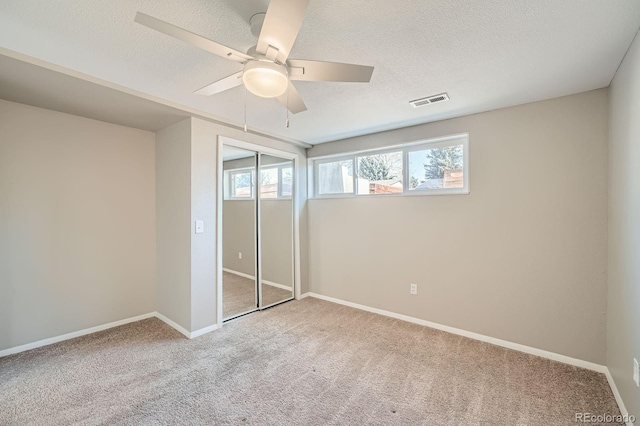 unfurnished bedroom featuring carpet, visible vents, a textured ceiling, and ceiling fan