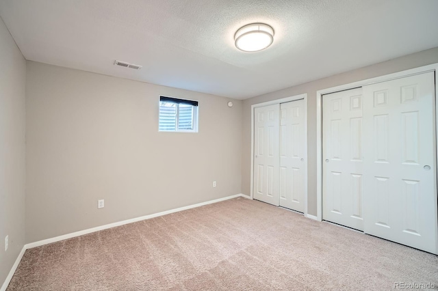 unfurnished bedroom featuring visible vents, baseboards, two closets, and carpet floors