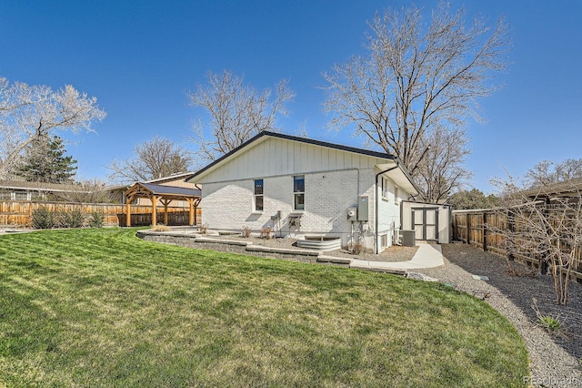 back of house featuring a yard, a fenced backyard, an outdoor structure, a storage unit, and brick siding