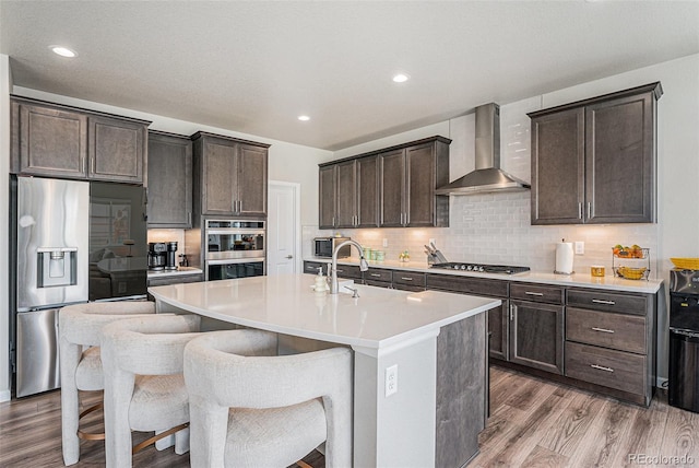 4532 Dewey Ln, Brighton, CO 80603 - kitchen featuring appliances with stainless steel finishes, wall chimney exhaust hood, wood finished floors, dark brown cabinets, and tasteful backsplash