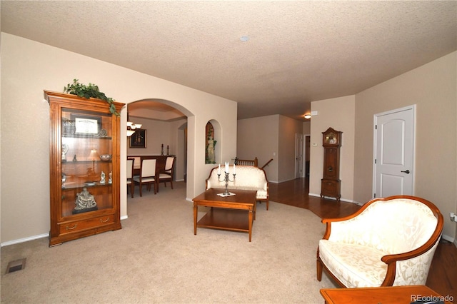 living area featuring arched walkways, carpet, visible vents, and a textured ceiling