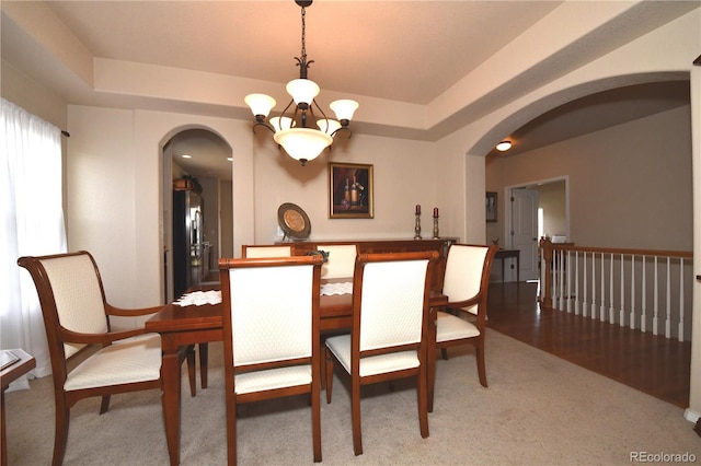 dining area with light carpet, arched walkways, a notable chandelier, and a raised ceiling