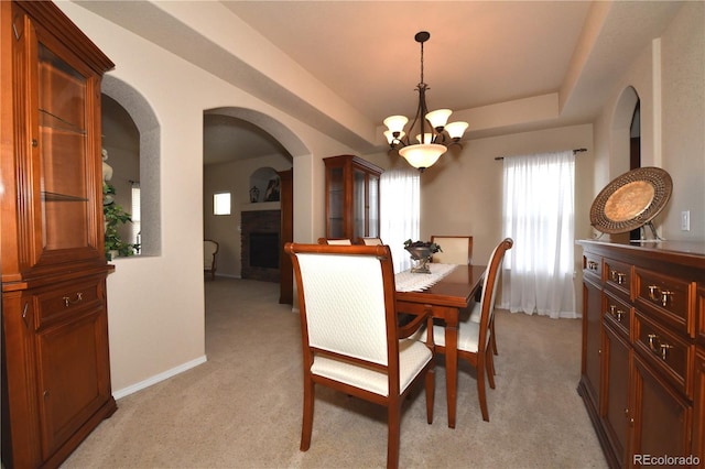 dining area featuring a fireplace, arched walkways, light colored carpet, a notable chandelier, and baseboards