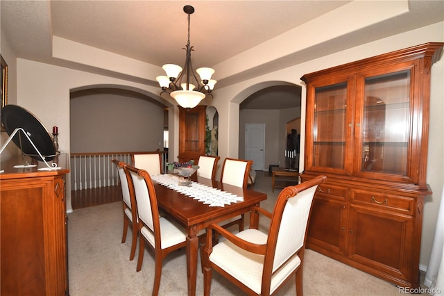 dining room with an inviting chandelier, a tray ceiling, arched walkways, and light colored carpet