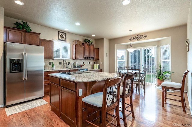 kitchen featuring light wood-style floors, stainless steel fridge, black electric cooktop, backsplash, and a kitchen island