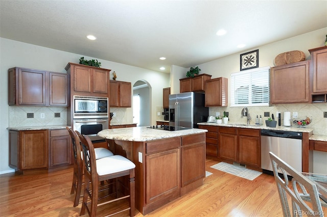 kitchen with stainless steel appliances, a sink, light wood-type flooring, decorative backsplash, and a kitchen island
