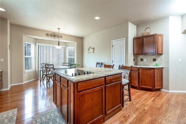 kitchen with brown cabinetry, a breakfast bar, light wood-type flooring, black electric stovetop, and decorative light fixtures