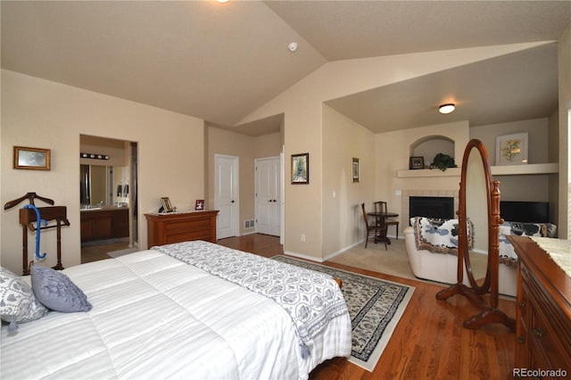 bedroom featuring ensuite bathroom, visible vents, vaulted ceiling, wood finished floors, and a tile fireplace