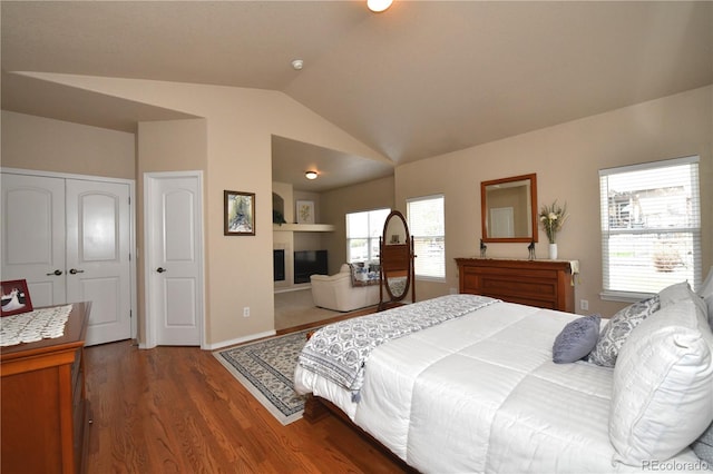 bedroom with a glass covered fireplace, wood finished floors, and lofted ceiling