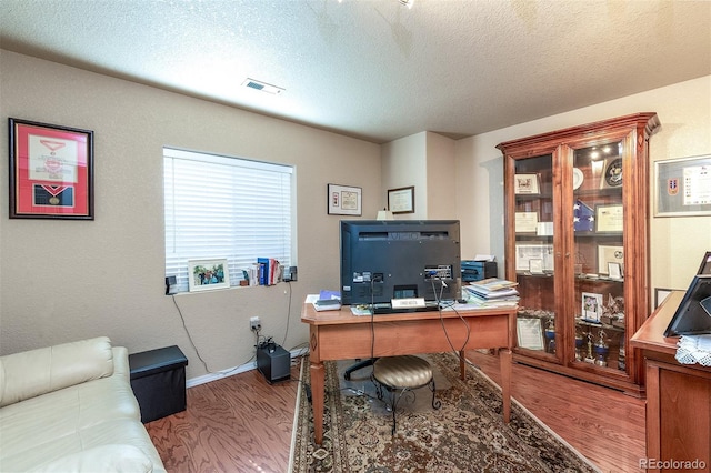 office with baseboards, visible vents, wood finished floors, and a textured ceiling