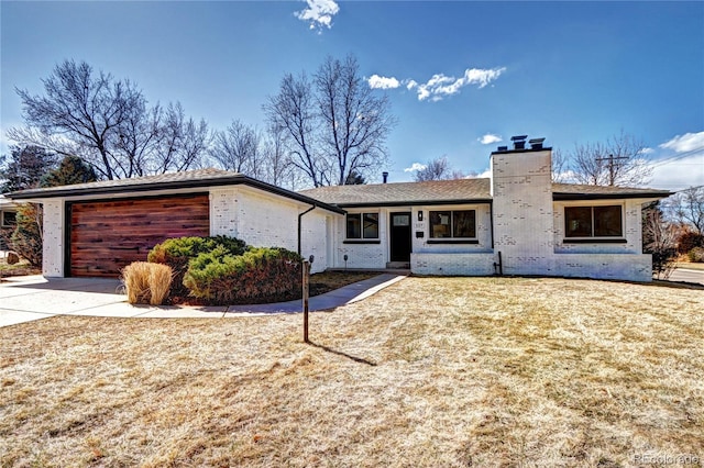 view of front of property featuring a front yard, driveway, a chimney, a garage, and brick siding