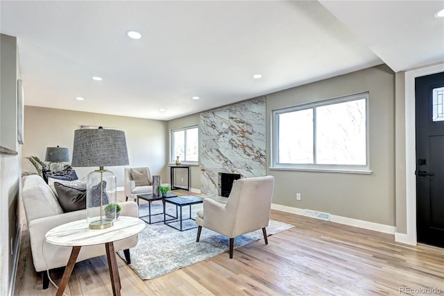 living area with baseboards, visible vents, light wood finished floors, a premium fireplace, and recessed lighting