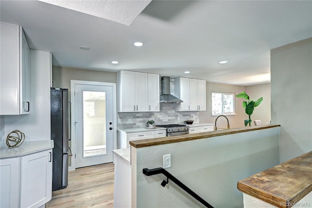 kitchen featuring light wood-type flooring, tasteful backsplash, freestanding refrigerator, gas stove, and wall chimney exhaust hood