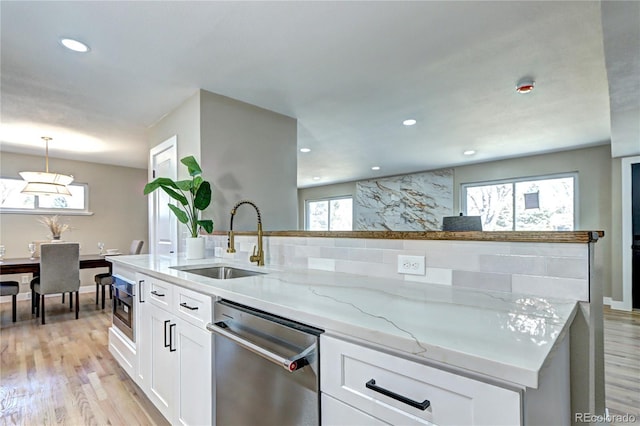 kitchen with light stone countertops, light wood-type flooring, stainless steel appliances, white cabinetry, and a sink