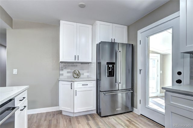 kitchen with light stone counters, decorative backsplash, appliances with stainless steel finishes, white cabinetry, and light wood-type flooring