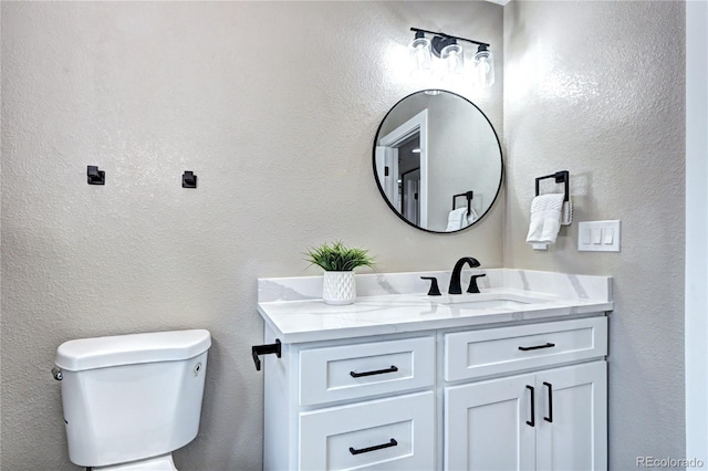 bathroom featuring toilet, vanity, and a textured wall