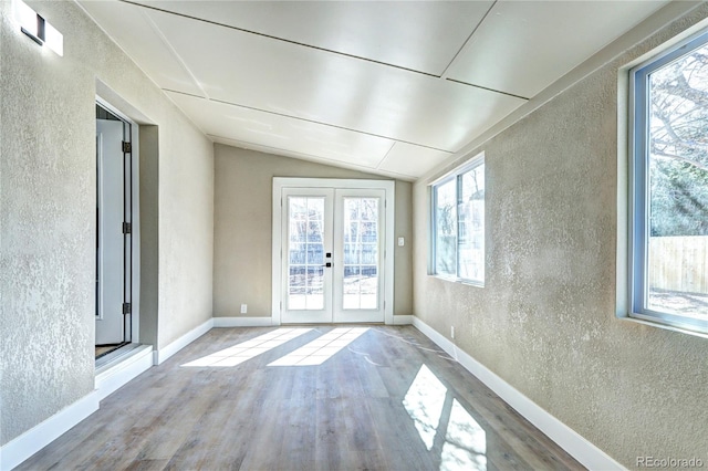 interior space featuring wood finished floors, a textured wall, french doors, baseboards, and vaulted ceiling