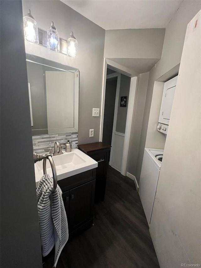 bathroom with tasteful backsplash, stacked washer and clothes dryer, vanity, and wood finished floors