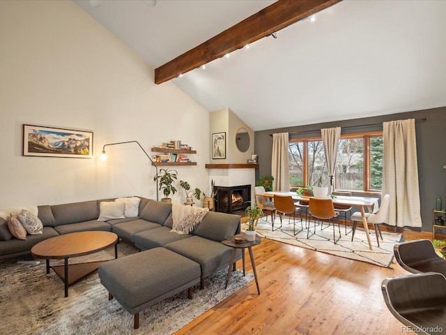 living room featuring high vaulted ceiling, a warm lit fireplace, beamed ceiling, and hardwood / wood-style floors