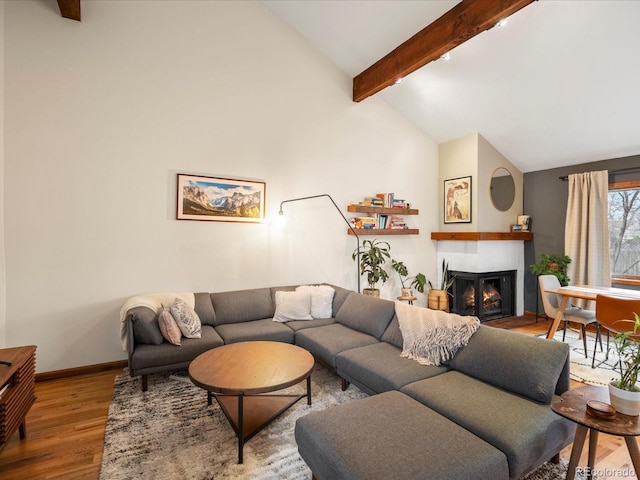 living area featuring a warm lit fireplace, baseboards, wood finished floors, beamed ceiling, and high vaulted ceiling