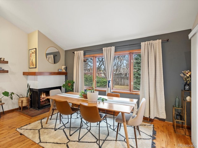 dining space featuring vaulted ceiling, a tiled fireplace, wood finished floors, and baseboards