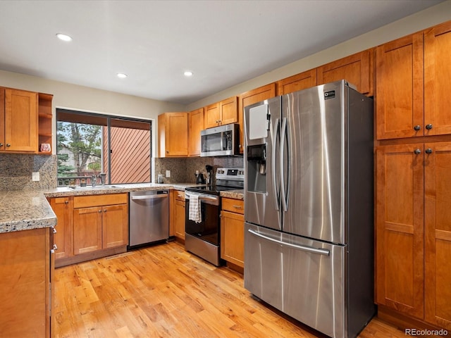 kitchen with open shelves, appliances with stainless steel finishes, light wood-style floors, brown cabinetry, and a sink