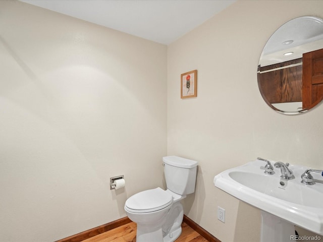 half bath featuring toilet, baseboards, a sink, and wood finished floors