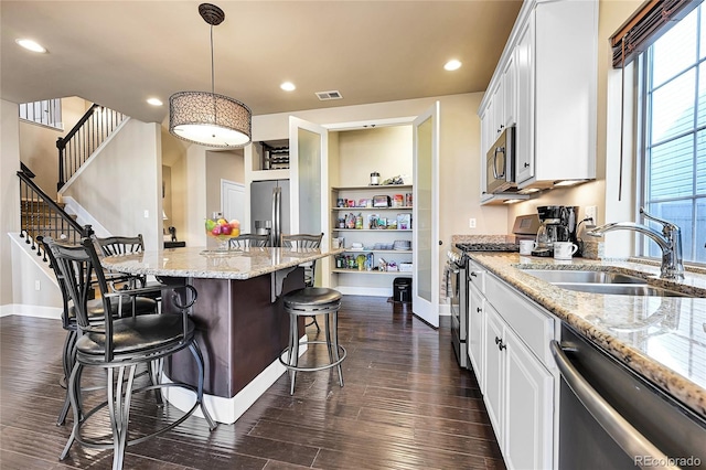 kitchen featuring visible vents, a kitchen bar, a sink, dark wood-style floors, and appliances with stainless steel finishes