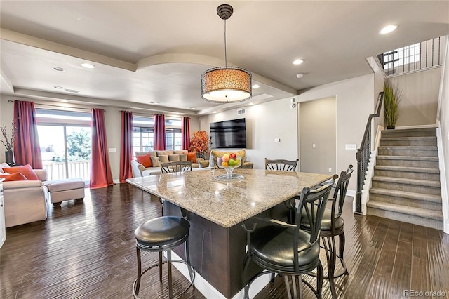 kitchen with a breakfast bar, dark wood-type flooring, light stone counters, and open floor plan