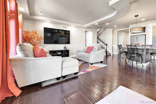 living area featuring stairs, a tray ceiling, visible vents, and dark wood-style flooring