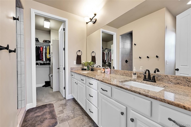 full bathroom featuring a walk in closet, double vanity, baseboards, and a sink