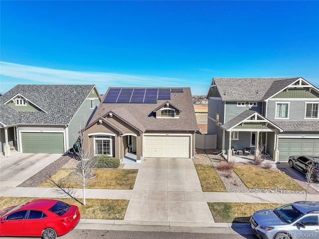 view of front facade with roof mounted solar panels, concrete driveway, a garage, and roof with shingles