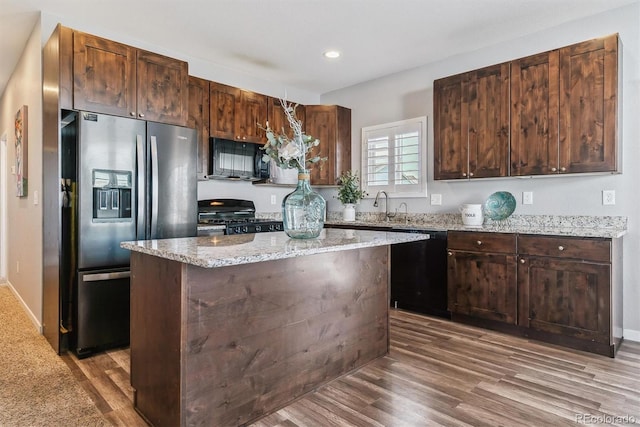 kitchen featuring black appliances, a kitchen island, light stone countertops, and hardwood / wood-style flooring