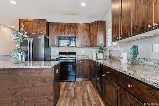 kitchen with sink, light stone counters, dark wood-type flooring, and black appliances