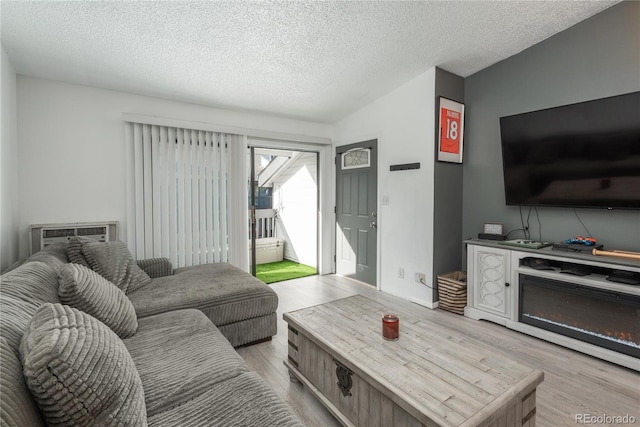 living room with lofted ceiling, light wood-style floors, a wall mounted air conditioner, and a textured ceiling