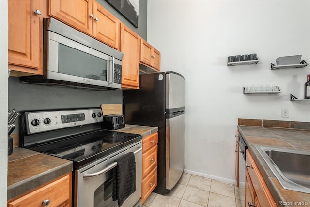 kitchen with baseboards, light tile patterned flooring, a sink, stainless steel appliances, and tile counters