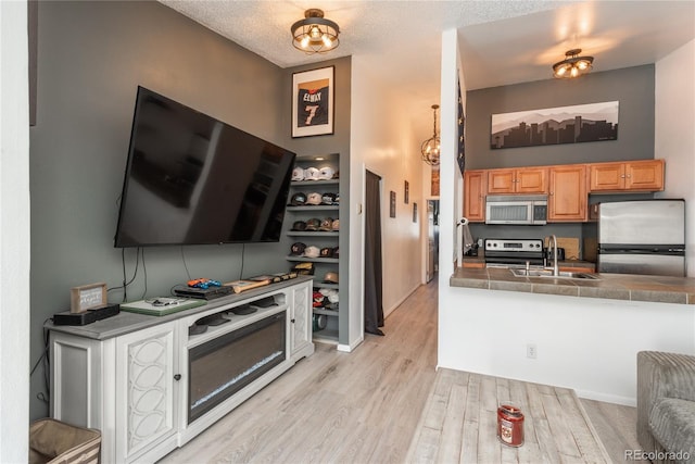 kitchen featuring a textured ceiling, light wood-style floors, appliances with stainless steel finishes, and a sink