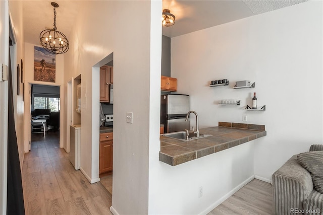 kitchen with freestanding refrigerator, a sink, tile counters, light wood-type flooring, and a chandelier