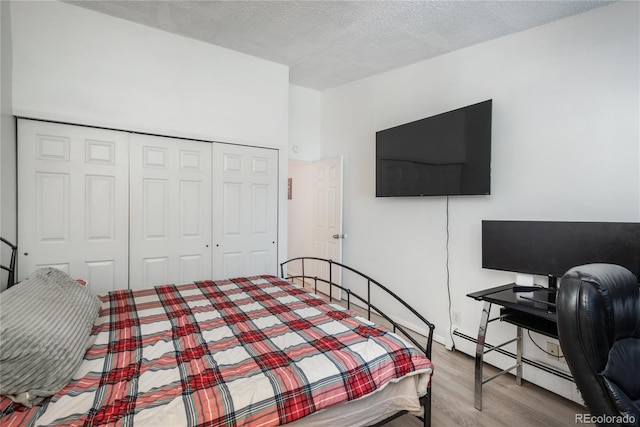 bedroom featuring a closet, a textured ceiling, baseboard heating, and wood finished floors