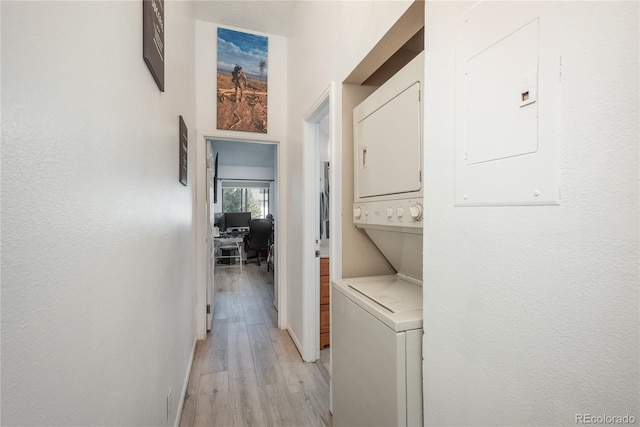 washroom featuring baseboards, light wood-type flooring, electric panel, laundry area, and stacked washer / drying machine