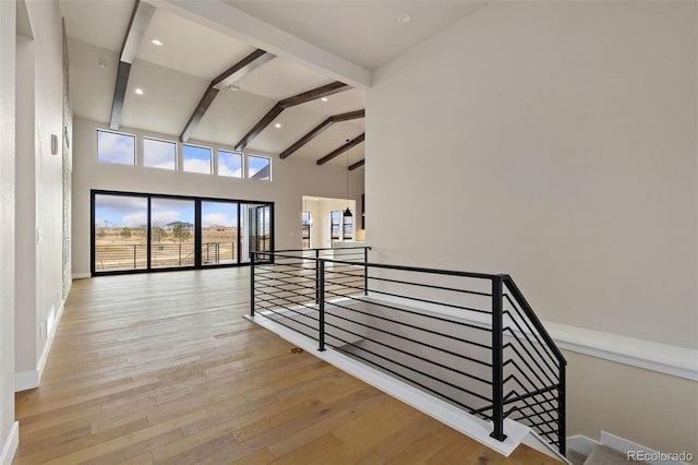 hallway with beam ceiling, light wood-type flooring, and a high ceiling