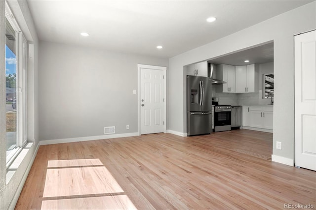 kitchen featuring light wood finished floors, visible vents, appliances with stainless steel finishes, white cabinets, and wall chimney exhaust hood