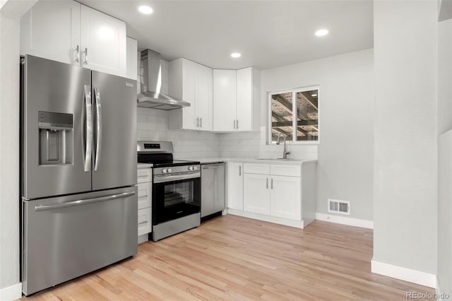 kitchen featuring stainless steel appliances, light countertops, white cabinetry, a sink, and wall chimney exhaust hood