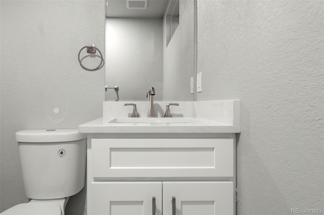 bathroom featuring visible vents, a textured wall, vanity, and toilet