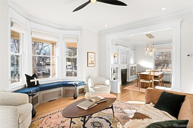 living room featuring ornamental molding, radiator, ceiling fan with notable chandelier, and light hardwood / wood-style flooring